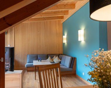 Gemütlicher Wohnbereich mit Holzverkleidung, Eckbank, türkiser Wand und Pendelleuchte – Bergheimat Ferienwohnungen in Obermaiselstein-Ried im Allgäu.