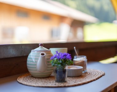Gemütliches Detail: Teekanne, Tassen und Veilchen auf einem Balkontisch – Bergheimat Ferienwohnungen in Obermaiselstein-Ried im Allgäu.