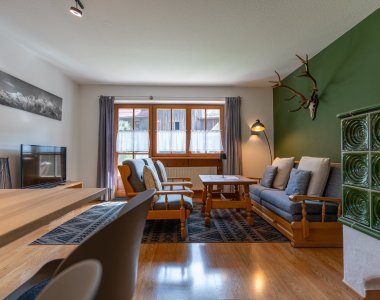 Großzügiges Wohnzimmer mit grünem Kachelofen, Sofa, Sesseln, Couchtisch und Hirschgeweih – Bergheimat Ferienwohnungen in Obermaiselstein-Ried im Allgäu.