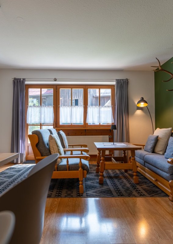Wohnzimmer mit Kachelofen und Sofa Großzügiges Wohnzimmer mit grünem Kachelofen, Sofa, Sesseln, Couchtisch und Hirschgeweih – Bergheimat Ferienwohnungen in Obermaiselstein-Ried im Allgäu.