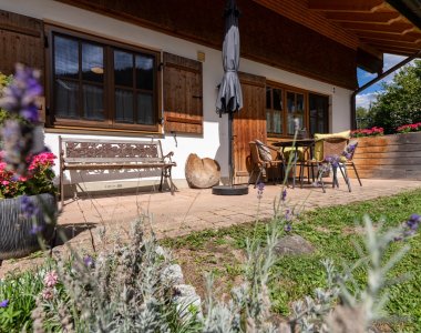 Sonnige Terrasse mit Holzbank, Sitzgruppe, Sonnenschirm, Lavendel und Blumenkübeln – Bergheimat Ferienwohnungen in Obermaiselstein-Ried im Allgäu.