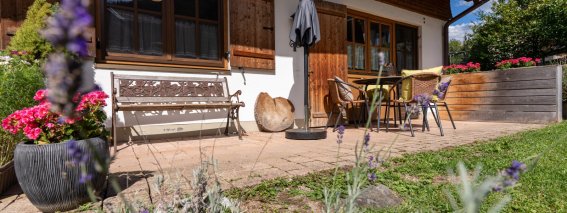Sonnige Terrasse mit Holzbank, Sitzgruppe, Sonnenschirm, Lavendel und Blumenkübeln – Bergheimat Ferienwohnungen in Obermaiselstein-Ried im Allgäu.