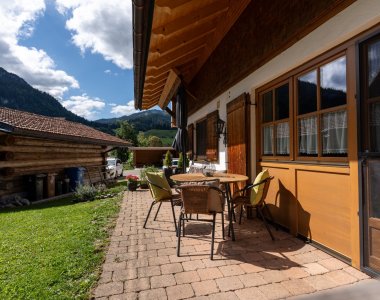 Gepflasterte Terrasse mit Tisch und Stühlen direkt vor der Wohnung, Blick auf Garten, Holzstadel und Berge – Bergheimat Ferienwohnungen in Obermaiselstein-Ried im Allgäu.