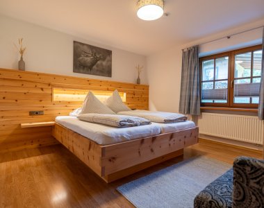 Gemütliches Schlafzimmer mit Doppelbett und Wandverkleidung aus Zirbenholz, Hirschbild und Fenster – Bergheimat Ferienwohnungen in Obermaiselstein-Ried im Allgäu.