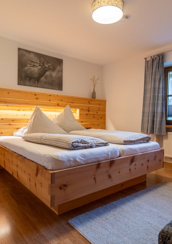 Schlafzimmer mit Zirbenholzbett Gemütliches Schlafzimmer mit Doppelbett und Wandverkleidung aus Zirbenholz, Hirschbild und Fenster – Bergheimat Ferienwohnungen in Obermaiselstein-Ried im Allgäu.