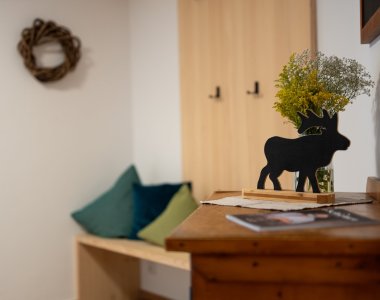 Liebevoll dekorierter Eingang mit Sitzbank, Kissen, Hirschfigur, Kranz und Wiesenblumen – Bergheimat Ferienwohnungen in Obermaiselstein-Ried im Allgäu.