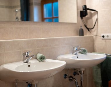 Gepflegtes Bad mit zwei Waschbecken, Spiegel, Föhn und Handtüchern – Bergheimat Ferienwohnungen in Obermaiselstein-Ried im Allgäu.