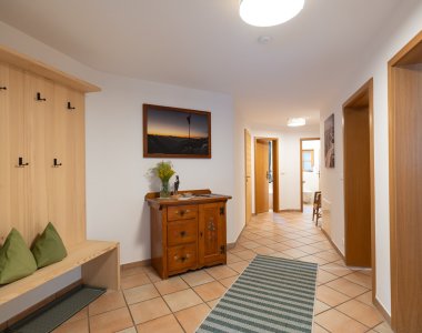 Heller Eingangsbereich mit Holzgarderobe, Sitzbank mit Kissen, Kommode und Fliesenboden – Bergheimat Ferienwohnungen in Obermaiselstein-Ried im Allgäu.