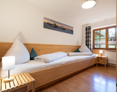 Freundliches Zimmer der Bergheimat Ferienwohnungen in Obermaiselstein-Ried mit Einzelbett aus Holz, Nachttisch und Bergpanorama-Bild an der Wand.