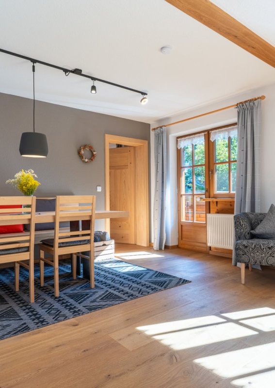 Essbereich mit Holztisch in moderner Ferienwohnung Moderner Essbereich der Bergheimat Ferienwohnungen in Obermaiselstein-Ried mit großem Holztisch, Stühlen, Teppich und Sessel am Fenster.