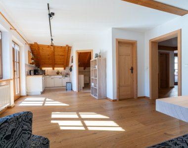 Offener, lichtdurchfluteter Wohnbereich einer Ferienwohnung der Bergheimat Ferienwohnungen in Obermaiselstein-Ried mit Holzboden und Blick in die Küche.