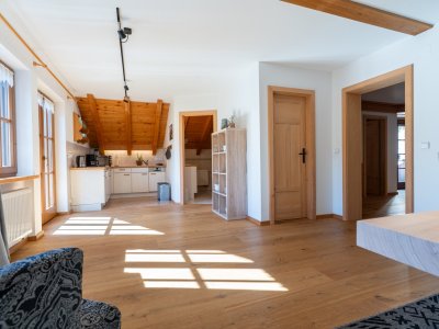 Offener, lichtdurchfluteter Wohnbereich einer Ferienwohnung der Bergheimat Ferienwohnungen in Obermaiselstein-Ried mit Holzboden und Blick in die Küche.