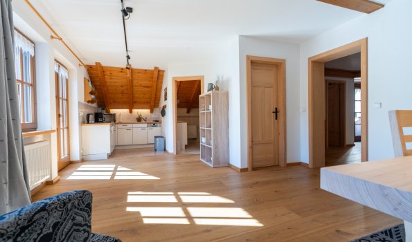 Offener, lichtdurchfluteter Wohnbereich einer Ferienwohnung der Bergheimat Ferienwohnungen in Obermaiselstein-Ried mit Holzboden und Blick in die Küche.