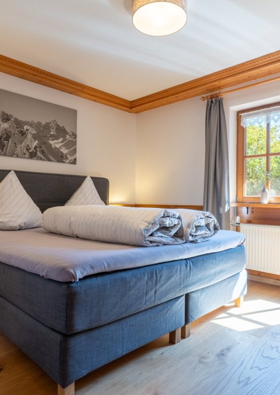 Schlafzimmer mit Boxspringbett und Balkontür Sonniges Schlafzimmer der Bergheimat Ferienwohnungen in Obermaiselstein-Ried mit Boxspringbett, Nachttischen, Bergbild und Tür zum Balkon.