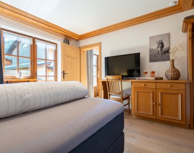 Wohn-Schlafraum der Bergheimat Ferienwohnungen in Obermaiselstein-Ried mit Bett, Fernseher, Holzkommode und Schreibtisch – auch ideal für Workation.
