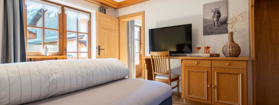 Wohn-Schlafraum der Bergheimat Ferienwohnungen in Obermaiselstein-Ried mit Bett, Fernseher, Holzkommode und Schreibtisch – auch ideal für Workation.