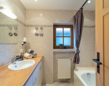 Helles Badezimmer der Bergheimat Ferienwohnungen in Obermaiselstein-Ried mit Badewanne, Waschtisch, Spiegel, Handtüchern und Fenster.