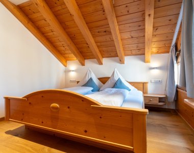 Gemütliches Dachschlafzimmer der Bergheimat Ferienwohnungen in Obermaiselstein-Ried mit sichtbaren Holzbalken und massivem Holz-Doppelbett.