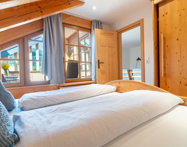 Helles Schlafzimmer der Bergheimat Ferienwohnungen in Obermaiselstein-Ried mit Doppelbett, Holzfenstern, Holztüren und Spiegel.