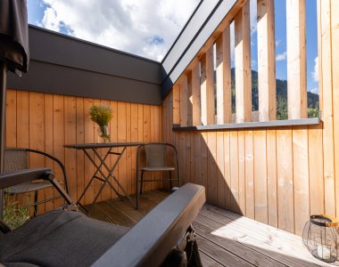Sonniger, windgeschützter Balkon mit Holzverkleidung, Bistrotisch und Stühlen in den Bergheimat Ferienwohnungen in Obermaiselstein-Ried.