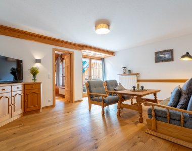 Heller Wohnbereich einer Ferienwohnung der Bergheimat Ferienwohnungen in Obermaiselstein-Ried: Holzboden, Sofa, Sessel, Couchtisch, Fernseher und Fenster zum Garten.