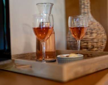 Zwei Gläser Roséwein und eine Karaffe auf einem Holztablett in den Bergheimat Ferienwohnungen in Obermaiselstein-Ried – Genussmoment im Urlaub.