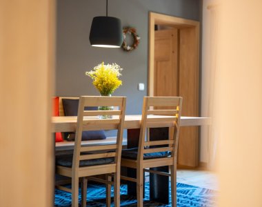 Blick in den Essbereich einer Ferienwohnung der Bergheimat Ferienwohnungen in Obermaiselstein-Ried: Holztisch mit Stühlen, Hängelampe und frischen gelben Blumen.