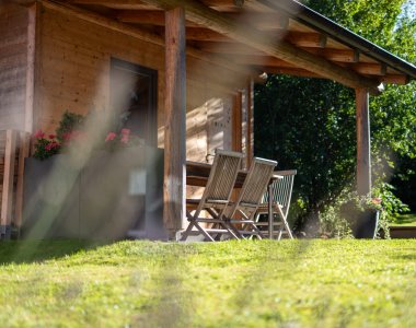 Gemütlicher, überdachter Holzpavillon im Garten der Bergheimat Ferienwohnungen in Obermaiselstein-Ried mit Stühlen und Blumen – ideal zum Entspannen im Grünen.
