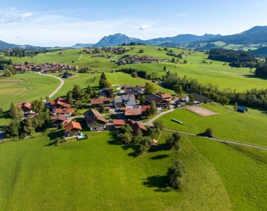 Weite Drohnenaufnahme über Obermaiselstein-Ried mit Häusern, sanften Wiesenhügeln und dem Bergpanorama der Allgäuer Alpen – die Ferienregion der Bergheimat Ferienwohnungen.