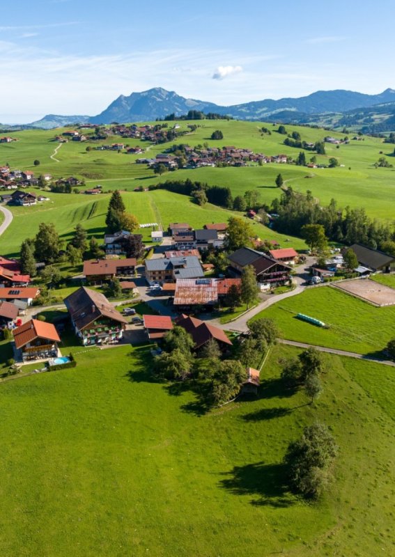 Panorama Obermaiselstein-Ried – Dorf, Wiesen und Allgäuer Alpen Weite Drohnenaufnahme über Obermaiselstein-Ried mit Häusern, sanften Wiesenhügeln und dem Bergpanorama der Allgäuer Alpen – die Ferienregion der Bergheimat Ferienwohnungen.