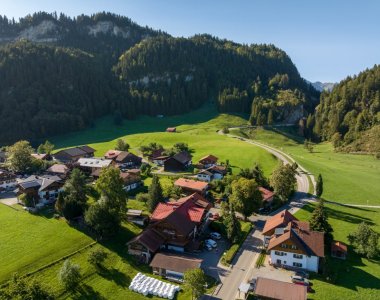 Drohnenaufnahme von Obermaiselstein-Ried im Oberallgäu: Allgäuer Häuser, grüne Almwiesen und bewaldete Berghänge an einem sonnigen Spätsommertag – Lage der Bergheimat Ferienwohnungen.