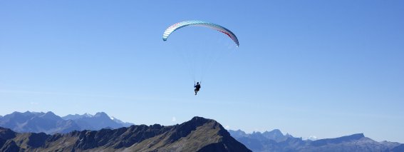 Gleitschirmflieger schwebt vor blauem Himmel über den Gipfeln der Allgäuer Alpen – Bergheimat Ferienwohnungen in Obermaiselstein-Ried im Allgäu.
