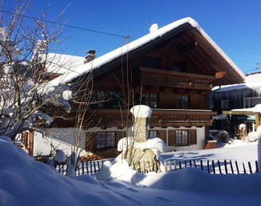 Ostansicht des traditionellen Holzhauses im tiefen Schnee unter blauem Winterhimmel – Bergheimat Ferienwohnungen in Obermaiselstein-Ried im Allgäu.