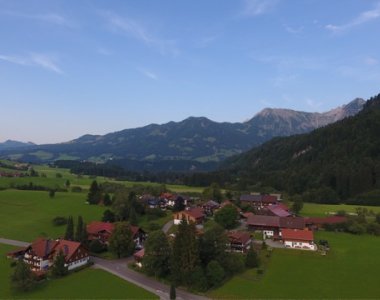 Luftaufnahme von Ried im Sommer mit Häusern, Wiesen, Wald und den Allgäuer Bergen im Hintergrund – Bergheimat Ferienwohnungen in Obermaiselstein-Ried im Allgäu.