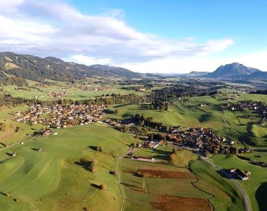 Luftaufnahme von Obermaiselstein und den umliegenden Wiesen mit Blick auf die Allgäuer Berge – Bergheimat Ferienwohnungen in Obermaiselstein-Ried im Allgäu.