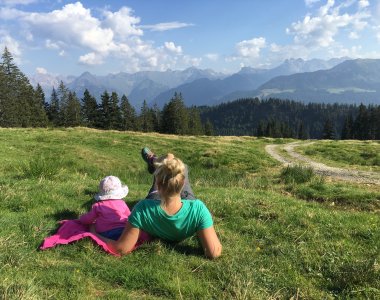Familie entspannt auf einer Bergwiese am Oberen Gund mit Blick auf das Bergpanorama der Allgäuer Alpen – Bergheimat Ferienwohnungen in Obermaiselstein-Ried im Allgäu.