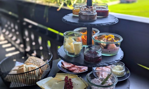 Ein köstliches Frühstück mit verschiedenen Speisen auf einem Balkon. Die Aussicht ist grün und lädt zum Entspannen ein.