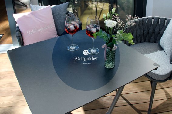 Auf einem Tisch stehen zwei Gläser mit Getränken und eine Blumenvase, einladende Atmosphäre im Freien.