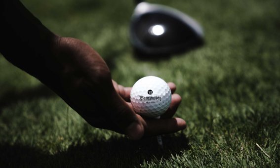 Ein Spieler hält einen Golfball auf dem Rasen bereit, während er sich auf den Abschlag vorbereitet.