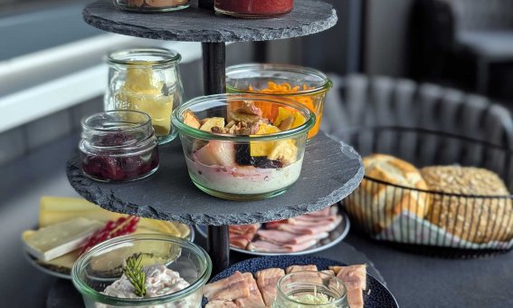 Auf einem eleganten Ständer sind verschiedene kleine Gerichte angerichtet. Es gibt Salate, Aufschnitt und Joghurt.