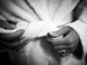 Zwei Hände binden einen weichen Morgenmantel und zeigen eine entspannte Atmosphäre am Morgen in einem gemütlichen Raum.