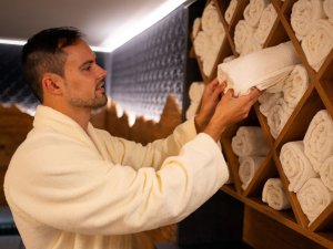 Ein Mann in einem Bademantel faltet Handtücher in einem modernen Wellnessbereich. Er arbeitet sorgfältig und konzentriert daran.