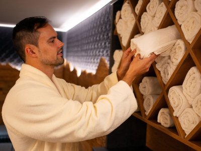 Ein Mann in einem Bademantel faltet Handtücher in einem modernen Wellnessbereich. Er arbeitet sorgfältig und konzentriert daran.