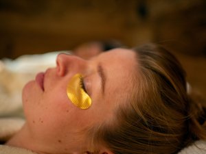 Eine Frau entspannt sich und nutzt eine goldene Augenmaske während einer Hautpflegebehandlung in einem ruhigen Raum.