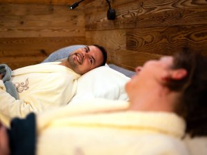 Zwei Personen liegen in Bademänteln auf Betten und genießen eine entspannte Zeit in einem Wellnessbereich.