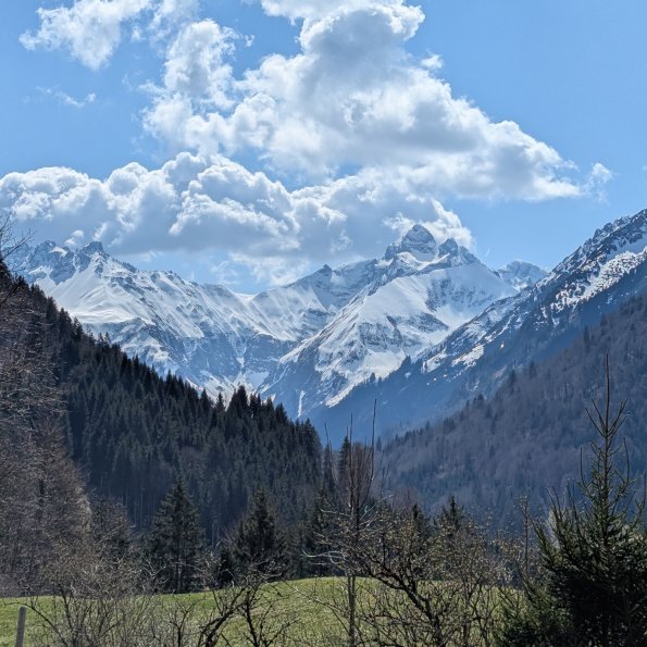 Die Aussicht zeigt schneebedeckte Berge und grüne Wiesen an einem klaren Tag in den Alpen im Frühling.