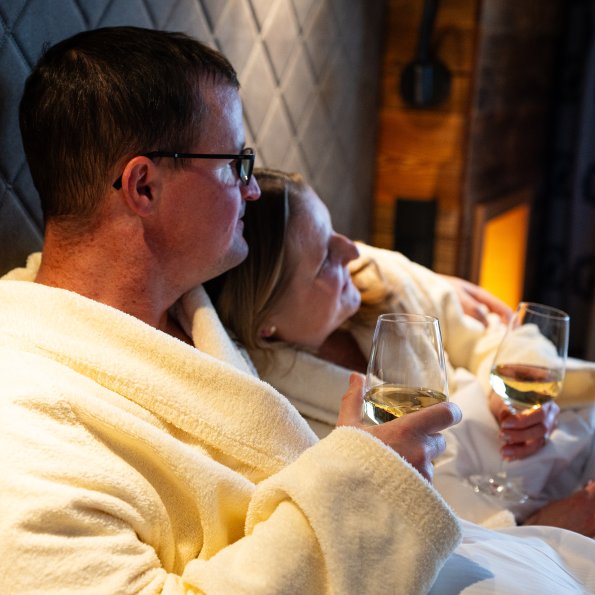 Entspannung in einem Hotelzimmer mit Getränken Ein Paar sitzt in einem Hotelzimmer und genießt Getränke. Sie tragen Bademäntel und relaxen im Bett.