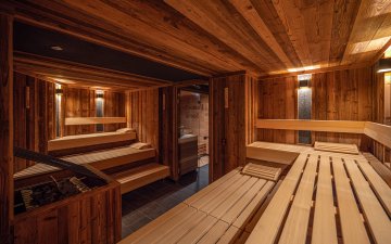 Gäste entspannen sich in einer gemütlichen Holzsauna mit warmem Licht und einladendem Ambiente. Perfekter Ort zum Relaxen.