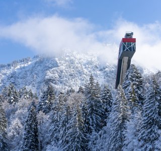 Die Sprungschanze in Oberstdorf ragt über schneebedeckte Bäume in einer winterlichen Berglandschaft.