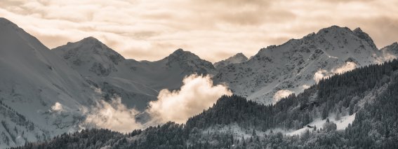 Die majestätischen Berge sind mit Schnee bedeckt, während Wolken über die Gipfel ziehen.